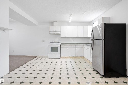 Kitchen featuring white cabinetry, white range, stainless steel refrigerator, and patterned floor tile - 2915 151A Avenue Nw, Edmonton, AB 