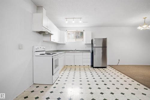 Bright, open kitchen featuring white cabinetry, stainless steel appliances including a refrigerator and electric range, and a distinctive geometric tile floor in black and white - 2915 151A Avenue Nw, Edmonton, AB 