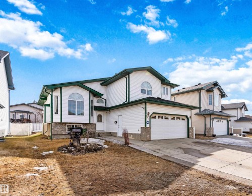 White siding exterior with green trim, arched windows, an attached two-car garage, and a concrete driveway - 2915 151A Avenue Nw, Edmonton, AB 