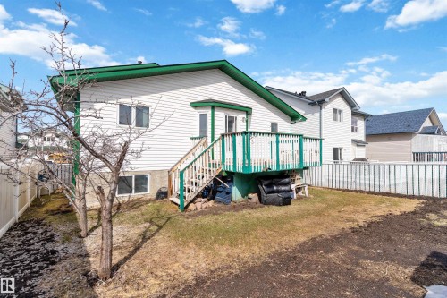 Rear exterior featuring white siding, a green-trimmed deck with stairs, a sliding glass door, and a white privacy fence - 2915 151A Avenue Nw, Edmonton, AB 