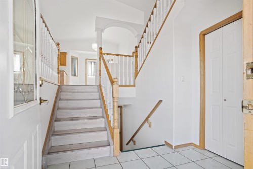 Foyer featuring tile flooring, wooden banister with white spindles, and a white paneled door - 2915 151A Avenue Nw, Edmonton, AB 