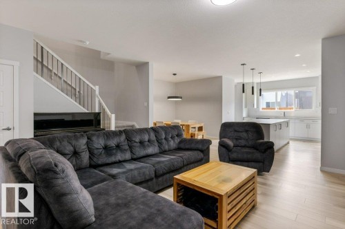 Open-concept living area featuring light wood-finish flooring, a white staircase with dark metal spindles, and contemporary recessed lighting - 7113 177A Avenue Nw, Edmonton, AB - Indoor Photo Showing Living Room