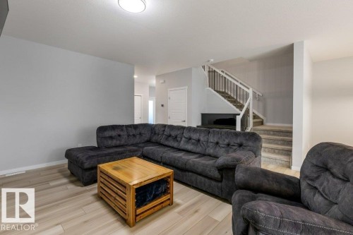 Spacious living area featuring light wood-finish flooring, a contemporary ceiling light fixture, and a stairway with white risers, carpeted treads, and a white railing with dark balusters - 7113 177A Avenue Nw, Edmonton, AB - Indoor Photo Showing Living Room