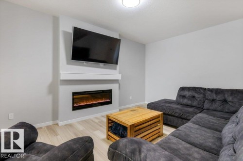 Living area featuring a contemporary electric fireplace with a white mantel, light wood-finish flooring, and a flush-mount ceiling light - 7113 177A Avenue Nw, Edmonton, AB - Indoor Photo Showing Living Room With Fireplace