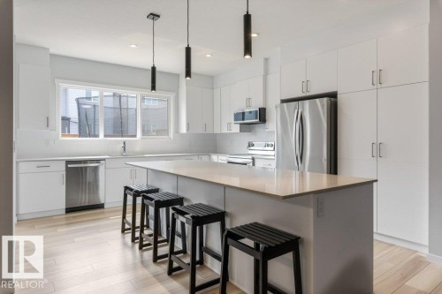 Contemporary kitchen featuring an oversized island with countertop seating, stainless steel appliances, extensive white cabinetry, a subway tile backsplash, and light wood-finish flooring - 7113 177A Avenue Nw, Edmonton, AB - Indoor Photo Showing Kitchen With Upgraded Kitchen