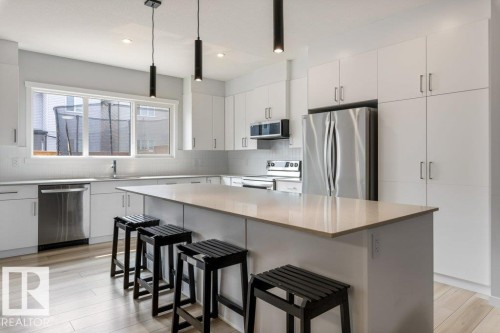 Contemporary kitchen featuring a large central island with a light-toned countertop, extensive white cabinetry, stainless steel appliances, a subway tile backsplash, and light wood-finish flooring - 7113 177A Avenue Nw, Edmonton, AB - Indoor Photo Showing Kitchen With Upgraded Kitchen