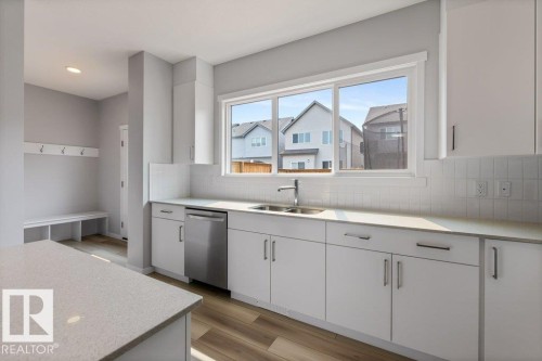 Contemporary kitchen featuring white cabinetry, light-colored countertops, a stainless steel dishwasher, and a double basin sink with a single-handle faucet - 7113 177A Avenue Nw, Edmonton, AB - Indoor Photo Showing Kitchen With Double Sink