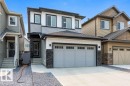 Contemporary exterior featuring multi-toned siding, a double-car garage with transom windows, a covered front entryway, and stone veneer accents - 7113 177A Avenue Nw, Edmonton, AB  - Outdoor With Facade 