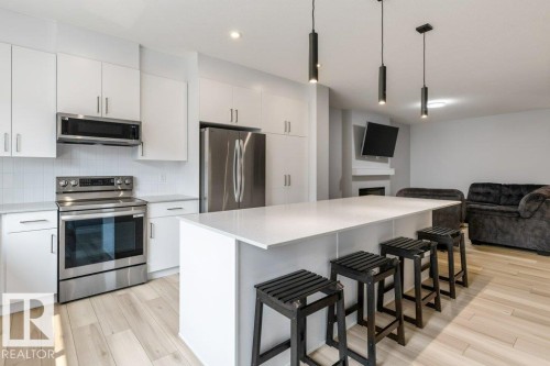 Open-concept kitchen featuring an island with counter seating, stainless steel appliances, white cabinetry, and wood-finish flooring - 7113 177A Avenue Nw, Edmonton, AB - Indoor Photo Showing Kitchen With Upgraded Kitchen