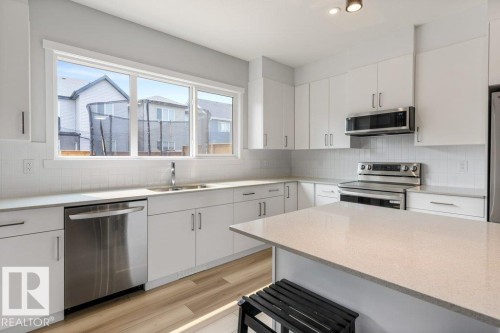 Modern kitchen featuring white cabinetry, light-colored countertops, stainless steel appliances, a subway tile backsplash, and wood-finish flooring - 7113 177A Avenue Nw, Edmonton, AB - Indoor Photo Showing Kitchen With Upgraded Kitchen