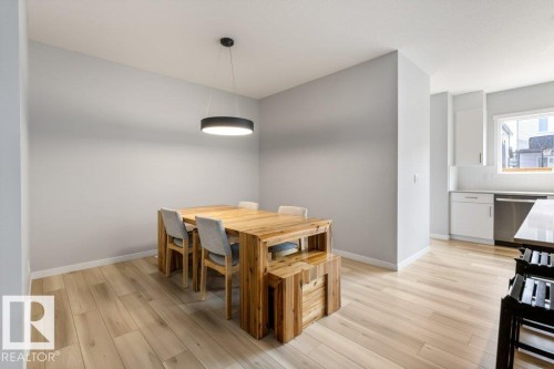 Dining area featuring wood-finish flooring, a modern circular pendant light, and light-toned wall paint - 7113 177A Avenue Nw, Edmonton, AB - Indoor Photo Showing Dining Room