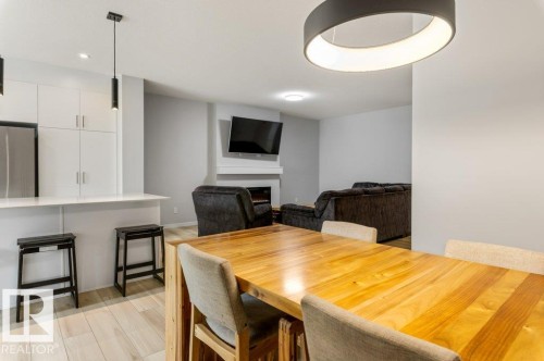 Open-concept living space featuring wood-finish flooring, a contemporary dining area with a circular pendant light, a kitchen island with seating, white cabinetry, and a fireplace with a mantel - 7113 177A Avenue Nw, Edmonton, AB - Indoor Photo Showing Dining Room