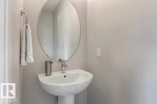 Pedestal sink featuring a chrome faucet, oval mirror, and light gray wall paint - 7113 177A Avenue Nw, Edmonton, AB - Indoor Photo Showing Bathroom
