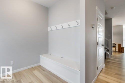 Entryway mudroom featuring a built-in white bench with storage, wall-mounted coat hooks, and light wood-finish flooring - 7113 177A Avenue Nw, Edmonton, AB - Indoor Photo Showing Other Room