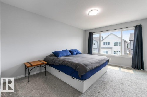 Spacious room with light gray walls, plush gray carpeting, and a large window featuring multiple panes - 7113 177A Avenue Nw, Edmonton, AB - Indoor Photo Showing Bedroom