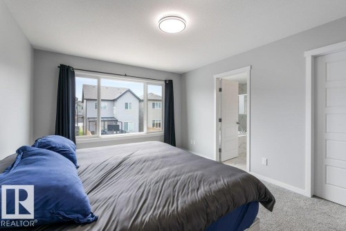 Room featuring a large multi-pane window, flush-mount ceiling light fixture, light gray carpeting, and white interior doors - 7113 177A Avenue Nw, Edmonton, AB - Indoor Photo Showing Bedroom