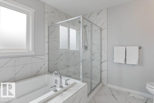 Bathroom featuring a built-in tub with chrome fixtures, a glass-enclosed shower, and white tiled walls and flooring with dark veining - 7113 177A Avenue Nw, Edmonton, AB - Indoor Photo Showing Bathroom