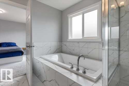 Built-in soaking tub with deck-mounted chrome fixtures, surrounded by large format marble-look tile - 7113 177A Avenue Nw, Edmonton, AB - Indoor Photo Showing Bathroom