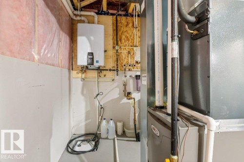Utility area featuring a tankless water heater, furnace, and exposed insulation - 7113 177A Avenue Nw, Edmonton, AB - Indoor Photo Showing Basement