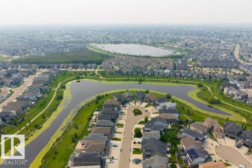 Aerial overview of a residential area featuring a curvilinear street layout and a central water feature with surrounding green spaces - 7113 177A Avenue Nw, Edmonton, AB - Outdoor With View