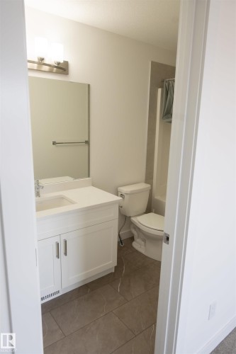 White vanity with integrated sink, rectangular mirror, brushed nickel light fixture, and large format tile flooring - #64 2710 66 St Sw Sw, Edmonton, AB 