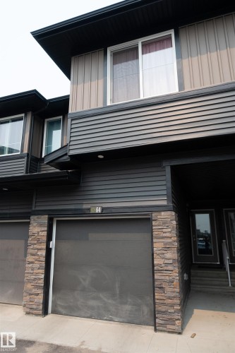 Contemporary exterior featuring dark horizontal siding, stone veneer accents, and a panel garage door - #64 2710 66 St Sw Sw, Edmonton, AB 