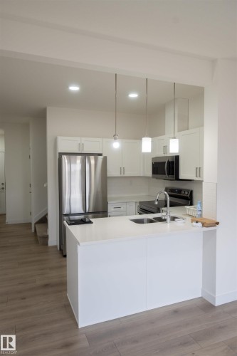 Kitchen featuring a center island, stainless steel appliances, white cabinetry, and wood-finish flooring - #64 2710 66 St Sw Sw, Edmonton, AB 