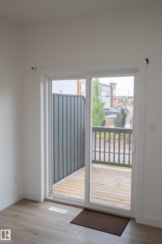 Wood-finish flooring, white walls, and a sliding glass door providing access to an exterior deck with wood flooring and dark railing - #64 2710 66 St Sw Sw, Edmonton, AB 