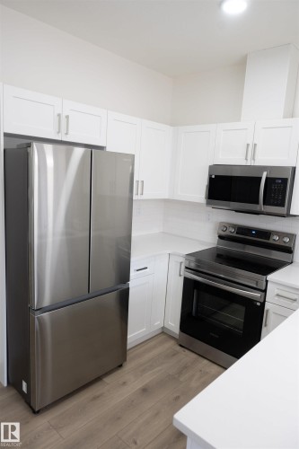 Modern kitchen with stainless steel appliances, white cabinetry, sleek countertops, and wood-finish flooring - #64 2710 66 St Sw Sw, Edmonton, AB 