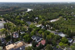 Aerial perspective showcasing a verdant neighborhood with a winding river, abundant mature trees, and a mix of residential properties - 