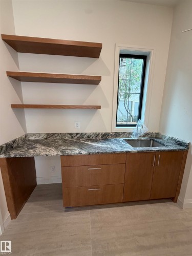 Built-in wood-finish cabinetry with silver hardware, stone countertop with integrated sink, three wood-finish floating shelves, and a tall window with black trim - 10223 130 Street Nw, Edmonton, AB 