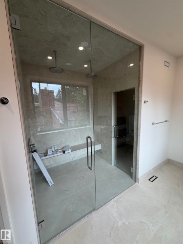 Spa-inspired primary bathroom featuring a frameless glass enclosure with polished chrome hardware, large-format tile flooring and wall surfaces, recessed ceiling lighting, and a soaking tub with integrated surround - 10223 130 Street Nw, Edmonton, AB 