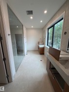 Contemporary bathroom featuring a spacious glass-enclosed shower, light-toned tile flooring, recessed ceiling lighting, and a large window - 