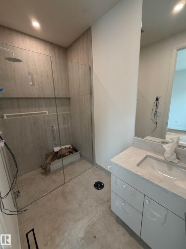 Glass-enclosed shower with a rainfall showerhead, tiled shower walls, built-in shower niche, and a vanity featuring an integrated sink and light-toned countertop - 10223 130 Street Nw, Edmonton, AB 