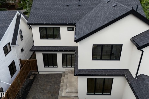 Exterior featuring light-colored siding, black-framed windows, dark shingle roofing, dark gutters, and a paver patio with a concrete step - 10223 130 Street Nw, Edmonton, AB 