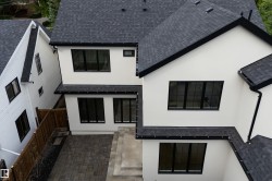 Exterior featuring light-colored siding, black-framed windows, dark shingle roofing, dark gutters, and a paver patio with a concrete step - 