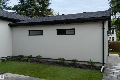 Exterior wall with two windows, dark roof, dark gutters, paved walkway, and maintained lawn with landscaping - 10223 130 Street Nw, Edmonton, AB 