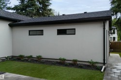 Exterior wall with two windows, dark roof, dark gutters, paved walkway, and maintained lawn with landscaping - 