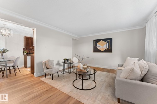 Light wood-finish flooring, crown molding, and a partial kitchen with dark wood cabinetry and tiled backsplash - #106 10735 81 Av Nw, Edmonton, AB 