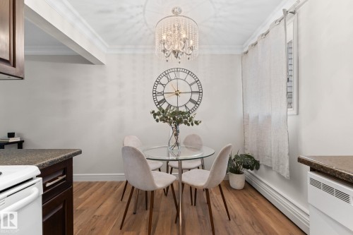 Hardwood-style flooring, crown molding, a built-in window with white shutters, and a crystal chandelier - #106 10735 81 Av Nw, Edmonton, AB 