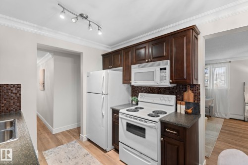 Kitchen featuring wood-finish cabinetry, built-in microwave, white electric range, and tile backsplash - #106 10735 81 Av Nw, Edmonton, AB 