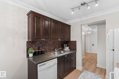 Dark wood-finish cabinetry, mosaic tile backsplash, double basin stainless steel sink, track lighting, and wood-finish flooring - #106 10735 81 Av Nw, Edmonton, AB 