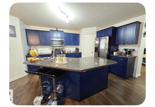 Kitchen featuring blue cabinetry, a central island with a granite countertop, stainless steel appliances, and wood-finish flooring - 8715 11 Avenue Sw, Edmonton, AB 