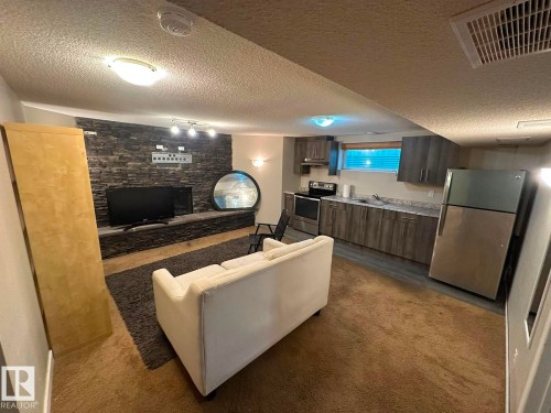 Stacked stone accent wall, recessed lighting, wood-finish kitchen cabinetry, stainless steel appliances, and a compact kitchen layout - 8715 11 Avenue Sw, Edmonton, AB 