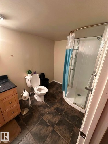 Bathroom featuring a corner shower, tiled flooring, built-in vanity with cabinetry, and a black countertop - 8715 11 Avenue Sw, Edmonton, AB 
