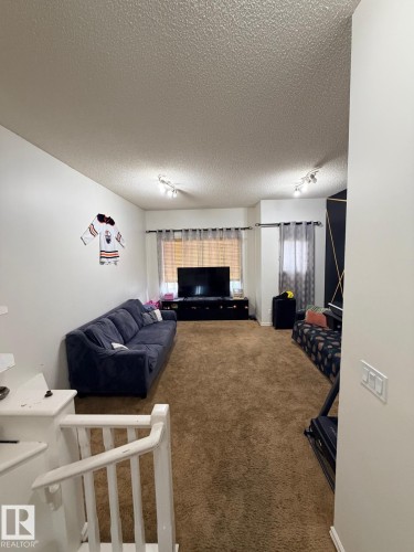 Recessed ceiling lighting, textured ceiling, brown carpeting, white interior walls, and a white staircase railing - 8715 11 Avenue Sw, Edmonton, AB 