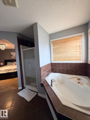Corner soaking tub with tiled surround, separate glass-enclosed shower, and tile flooring - 8715 11 Avenue Sw, Edmonton, AB 