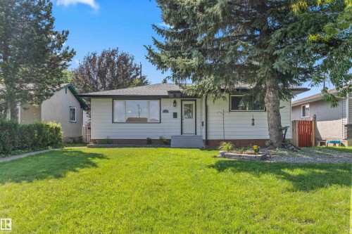 Single-story residence featuring white siding, a dark roof, and a prominent mature evergreen tree - 13320 123 Street Nw, Edmonton, AB - Outdoor