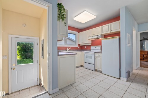 Kitchen featuring white cabinetry, white appliances, a white tile floor, and a rear door with a window providing exterior light - 13320 123 Street Nw, Edmonton, AB - Indoor Photo Showing Kitchen