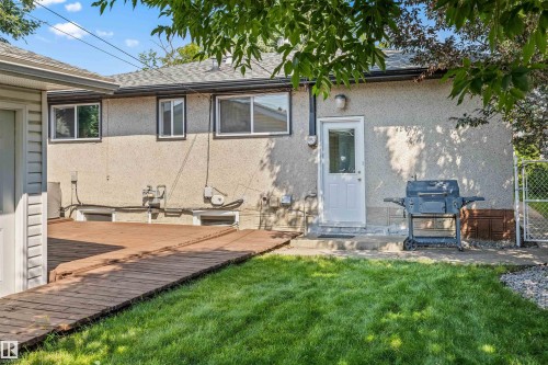 Rear exterior featuring stucco siding, multiple windows with dark trim, a white entry door, and a brown wood-finish deck - 13320 123 Street Nw, Edmonton, AB - Outdoor